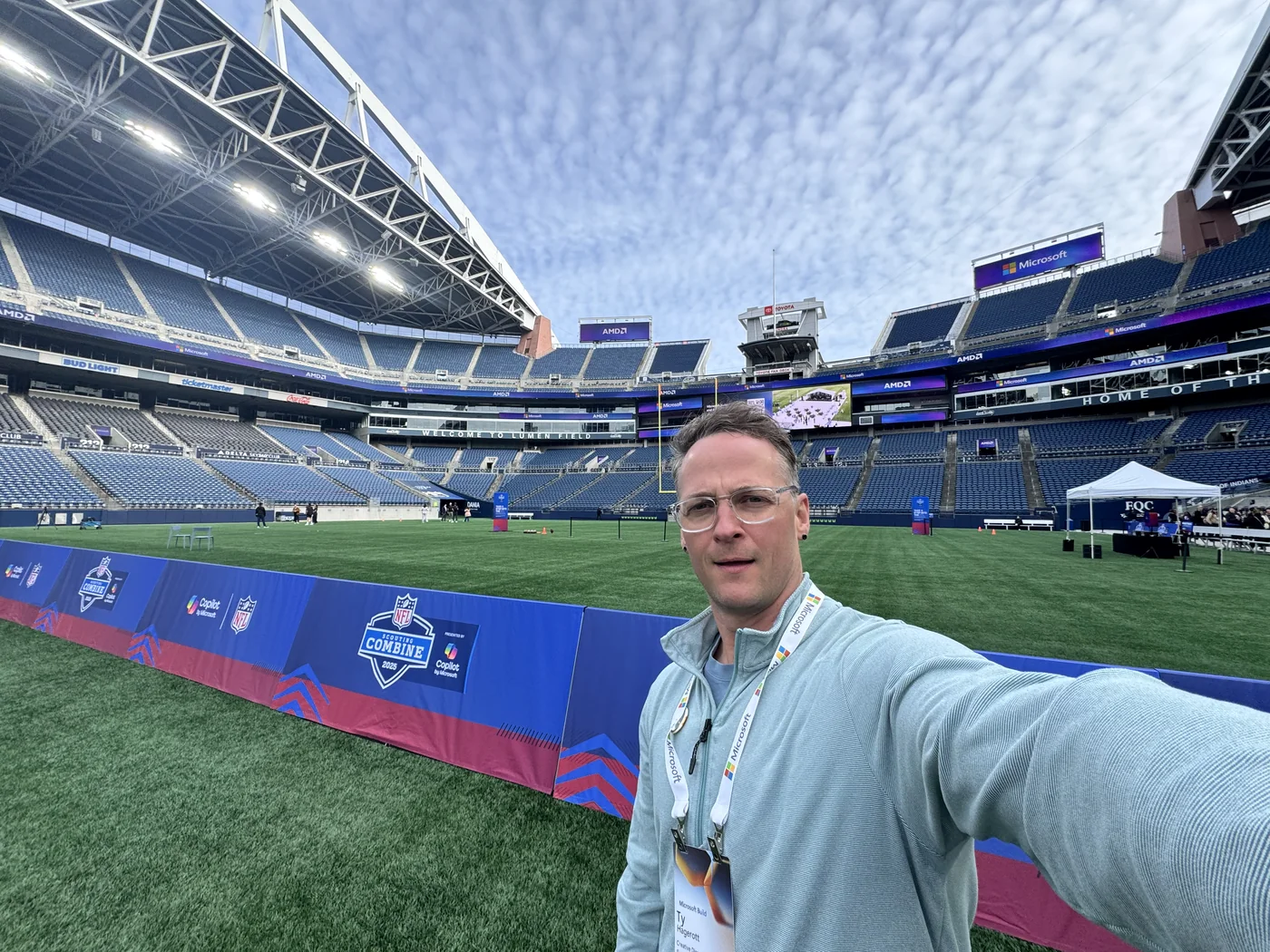 Ty Hagerott taking a selfie beside the field at Lumen Field, with stadium seating behind him